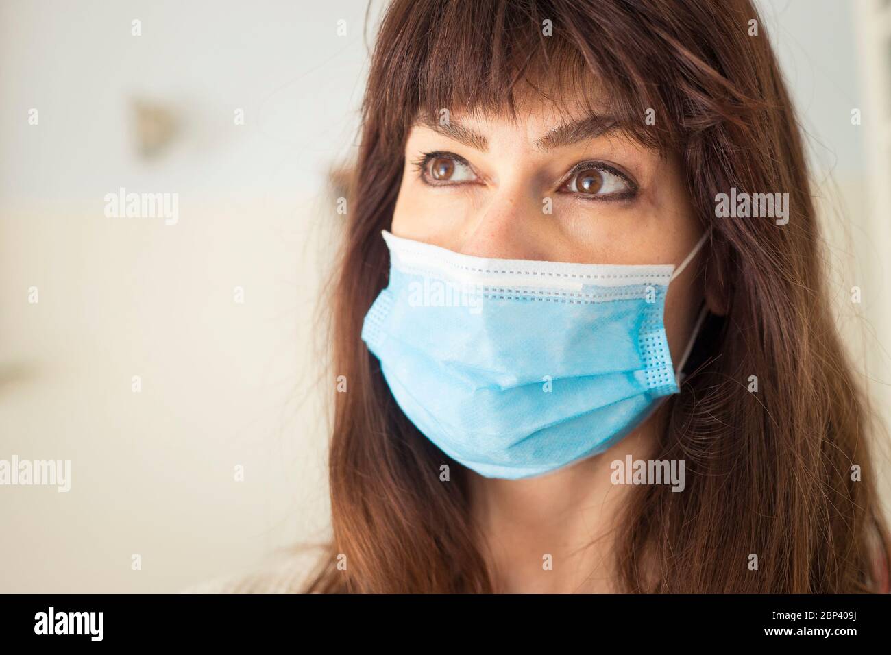 Femme caucasienne attirante avec de longs cheveux et des langes, portant un masque chirurgical bleu pendant une pandémie de covid-19 ou de coronavirus. Banque D'Images