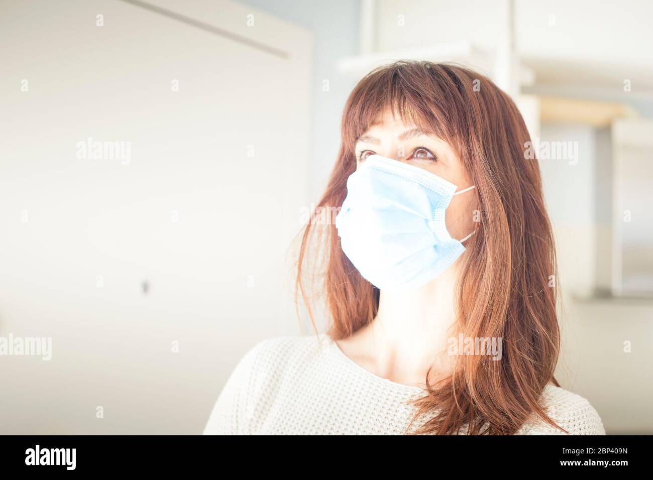Femme caucasienne attirante avec de longs cheveux et des langes, portant un masque chirurgical bleu pendant une pandémie de covid-19 ou de coronavirus. Copier l'espace sur la gauche. Banque D'Images