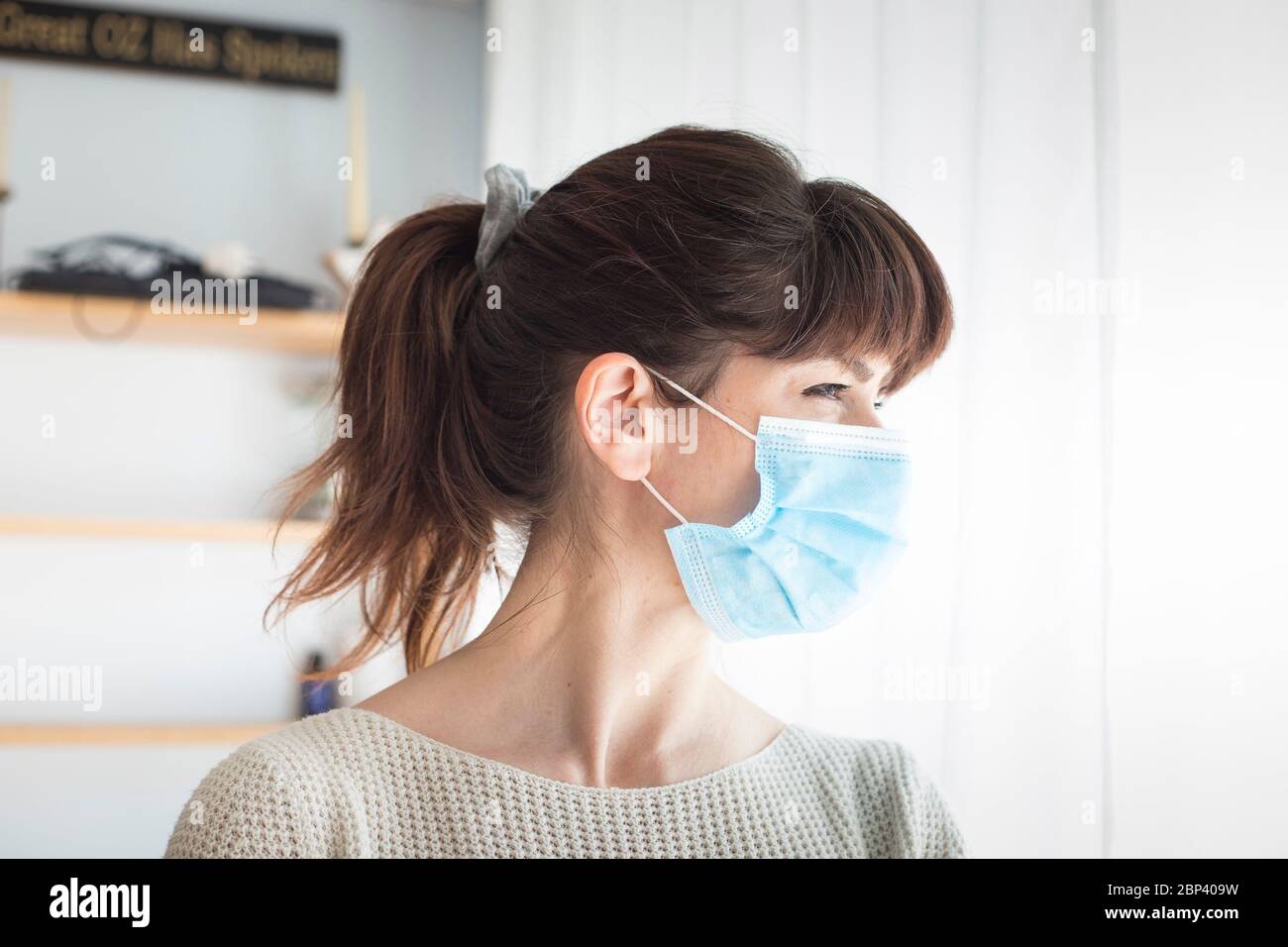 Femme caucasienne attirante avec queue de cheval et bangs, portant un masque chirurgical bleu pendant une pandémie de covid-19 ou de coronavirus. Portrait de profil. Banque D'Images