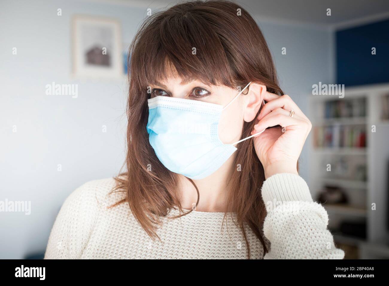 Caucasienne femme attirante avec de longs cheveux et des langes, mettant sur un masque chirurgical bleu pendant la pandémie de covid-19 ou de coronavirus. Banque D'Images