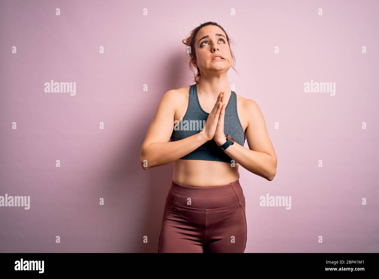 Jeune sportif blond faisant du sport porter des vêtements de sport sur fond rose mendier et prier avec les mains avec l'expression de l'espoir sur Banque D'Images