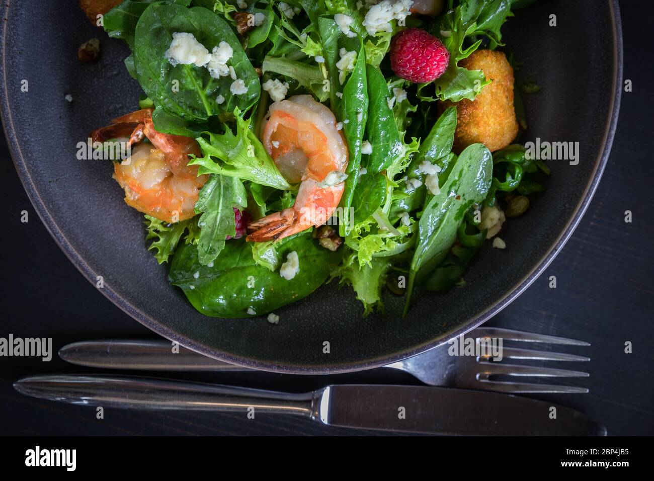 Vue rapprochée sur la salade de crevettes tigrées avec fromage de brie, framboises, noix. Panneau en bois sur fond gris Banque D'Images