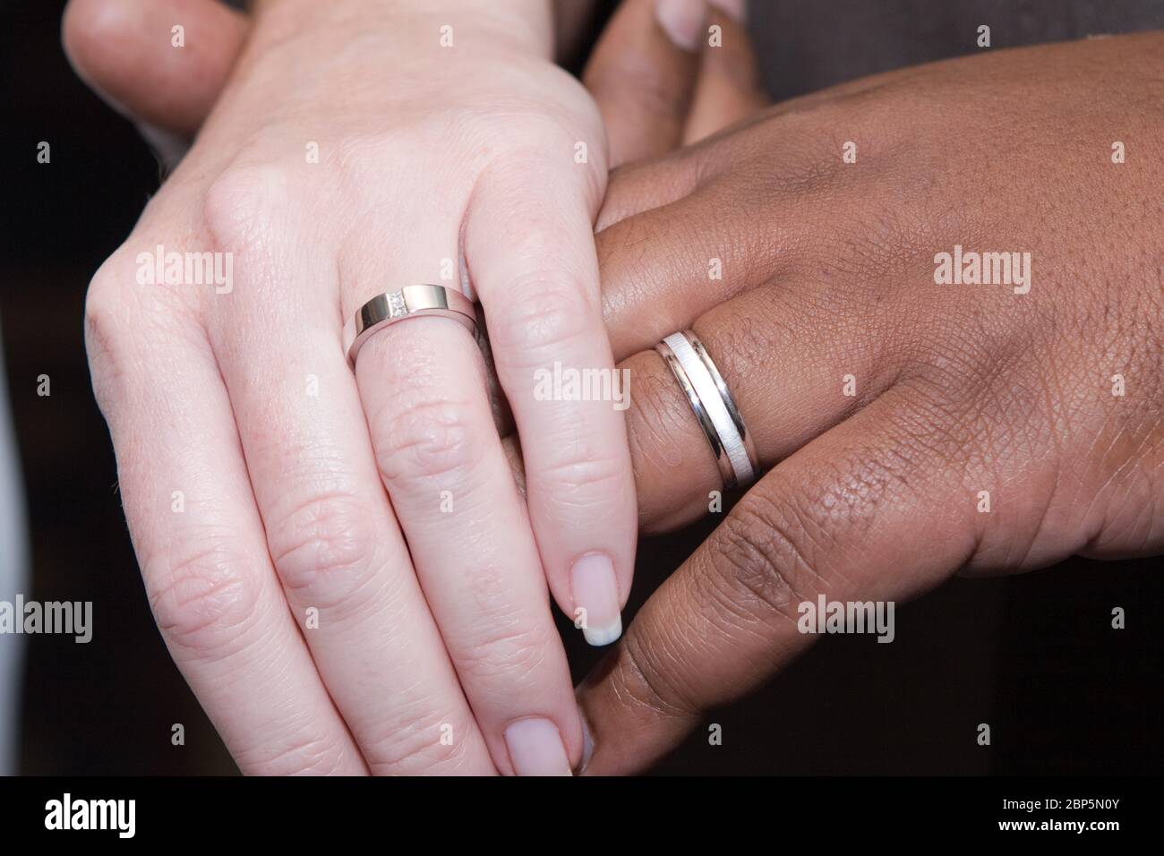 Gros plan sur un couple interracial tenant les mains et montrant des anneaux de mariage modestes. Banque D'Images