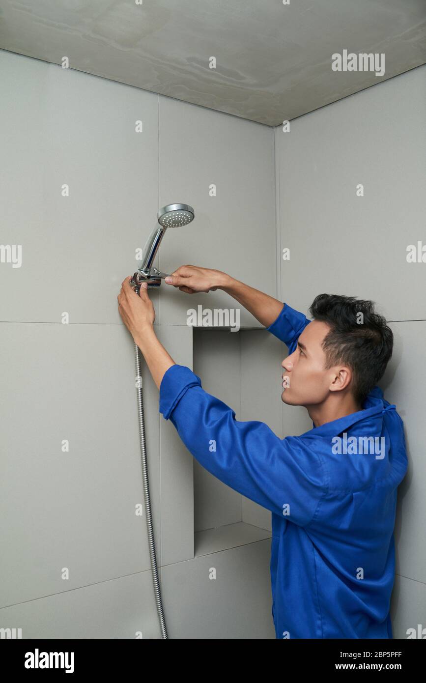 Sérieux plombier vietnamien dans la fixation uniforme fuite de la pomme de douche dans la salle de bains Banque D'Images