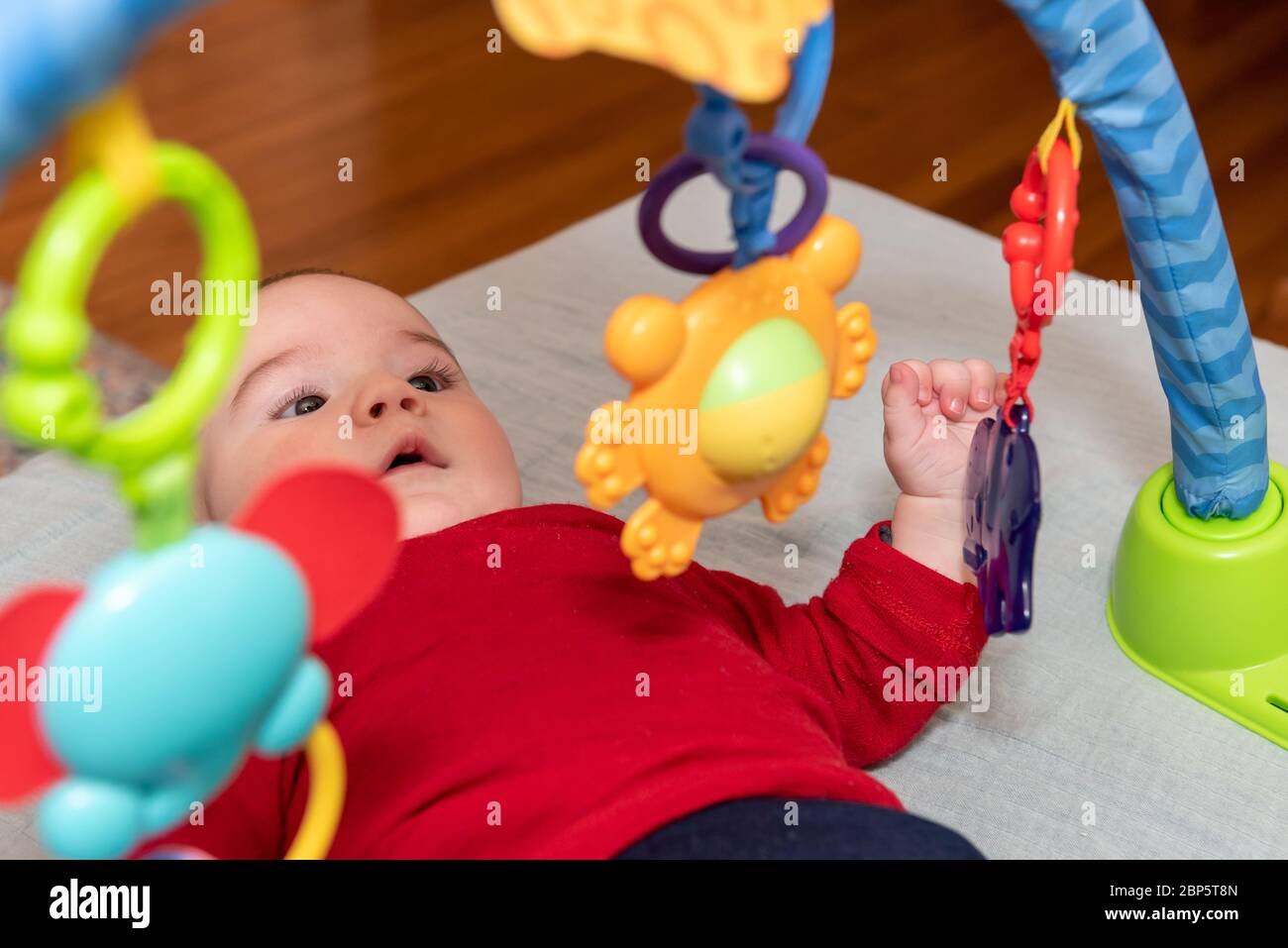 Adorable petit garçon de 6 mois sur le dos entouré de jouets colorés Banque D'Images