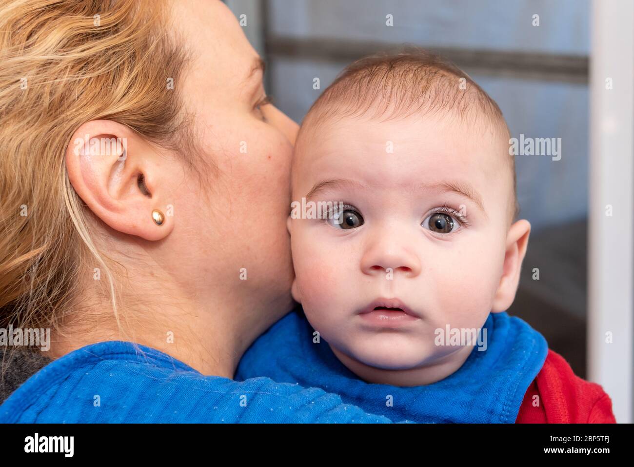 Mignon 6 mois petit garçon avec la curiosité expression sur son visage dans ses bras de mères Banque D'Images