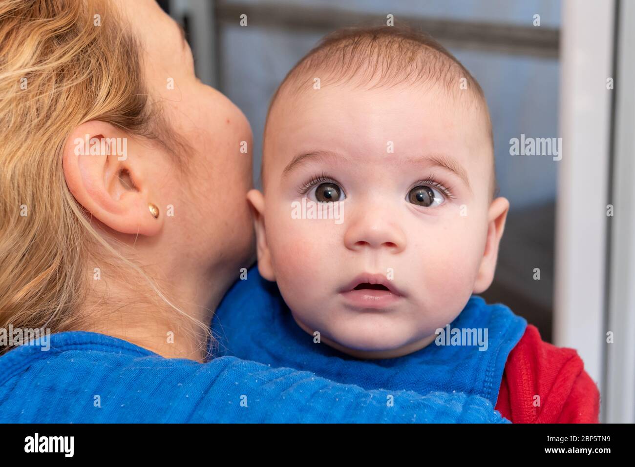Mignon 6 mois petit garçon avec la curiosité expression sur son visage dans ses bras de mères Banque D'Images