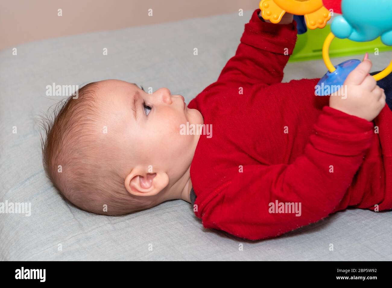 Adorable petit garçon de 6 mois sur le dos entouré de jouets colorés Banque D'Images