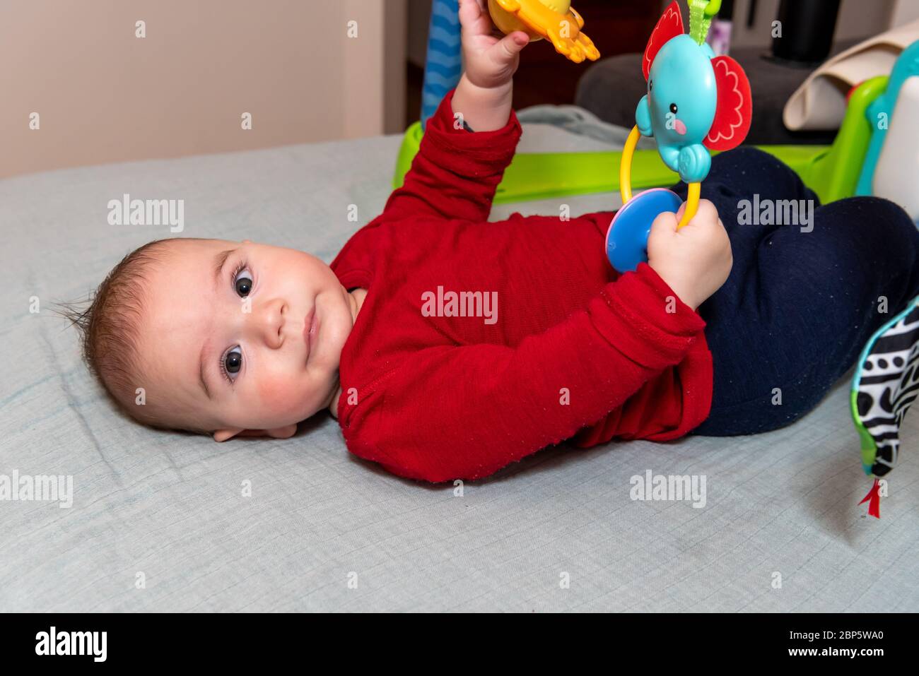 Adorable petit garçon de 6 mois sur le dos entouré de jouets colorés Banque D'Images