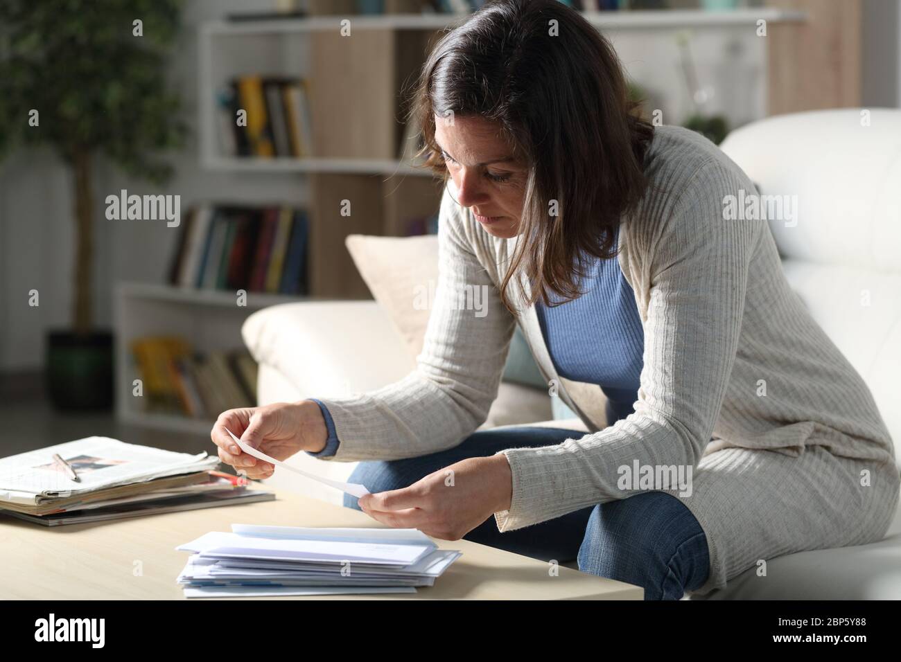Femme adulte vérifiant les reçus à la maison assis dans le canapé dans la salle de séjour la nuit Banque D'Images