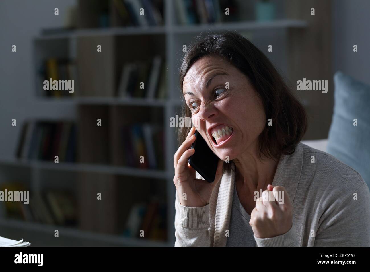 Une femme adulte en colère qui appelle sur un smartphone, assise dans le salon la nuit à la maison Banque D'Images