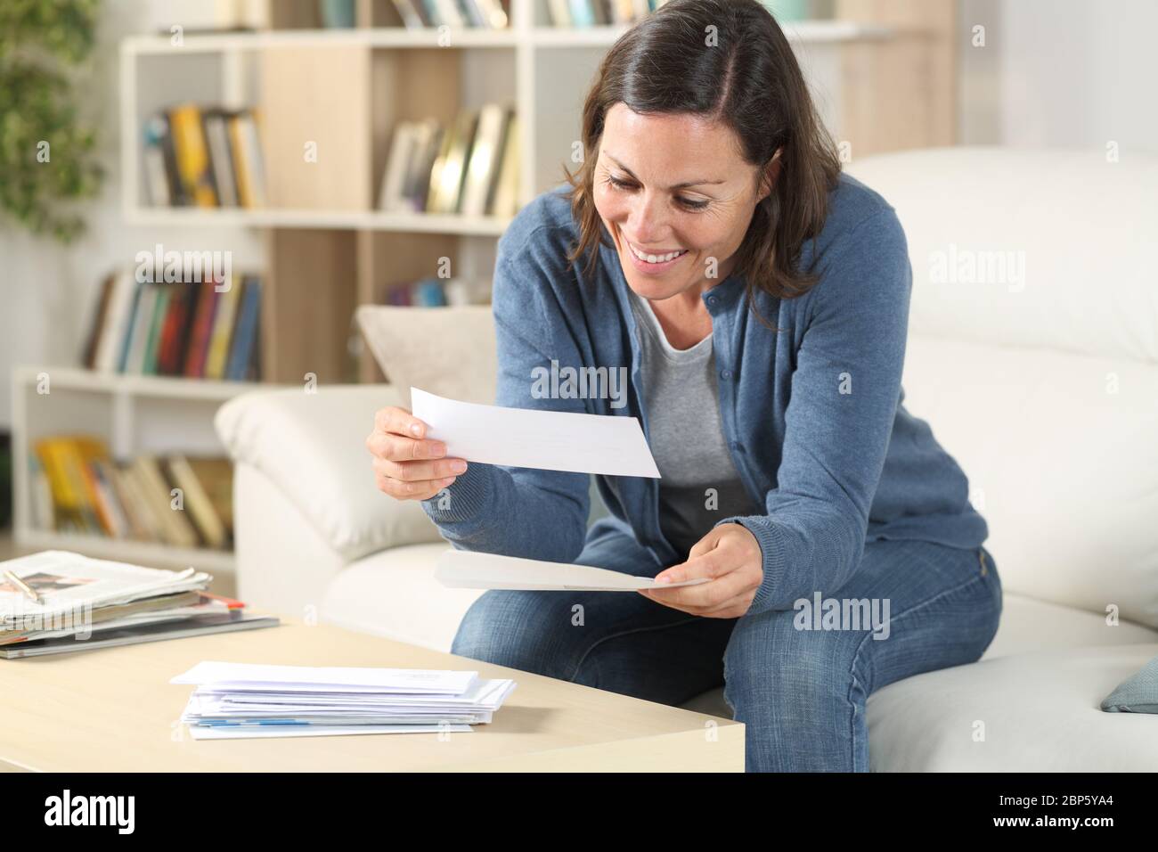 Bonne femme d'âge moyen regardant les reçus assis dans le salon à la maison Banque D'Images