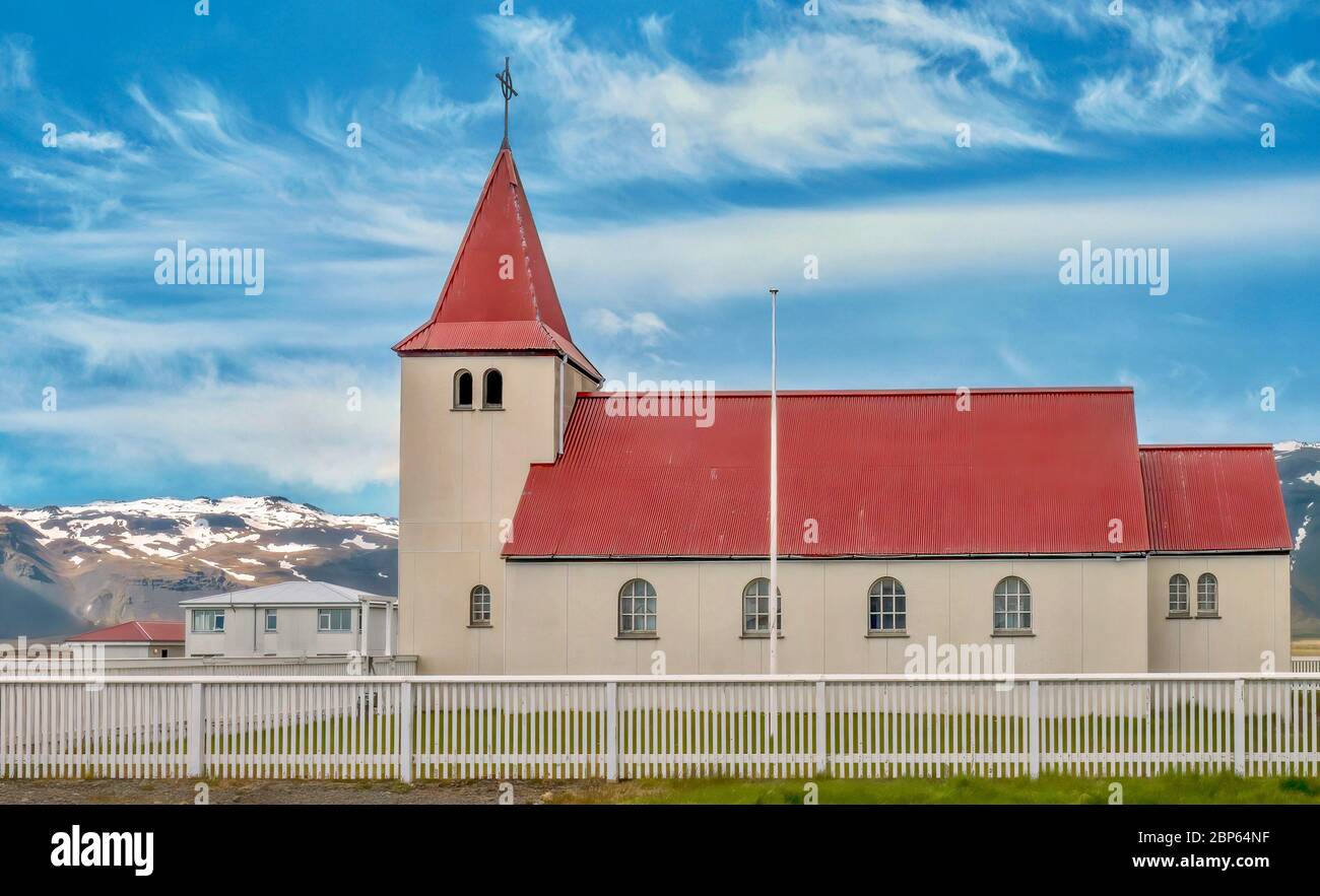 Une église rurale typique de l'ouest de l'Islande, avec des lignes simples et propres et un toit rouge, et des collines enneigées en arrière-plan. Banque D'Images