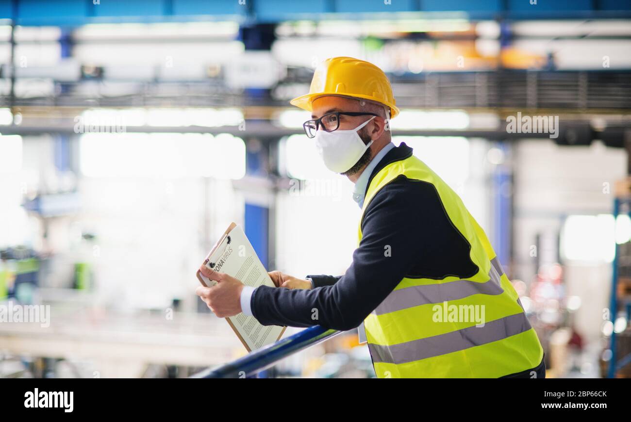 Technicien ou ingénieur avec masque de protection et casque debout en usine. Banque D'Images