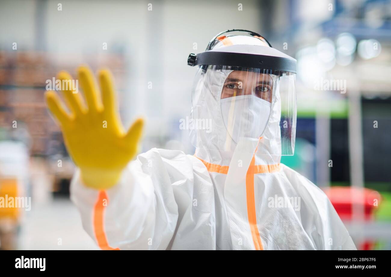 Travailleur avec masque de protection et combinaison dans l'usine industrielle, stop signe mouvement de main. Banque D'Images