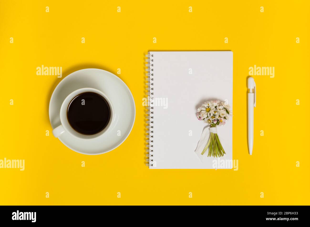 Tasse de café noir, carnet avec papier vierge, stylo et bouquet de fleurs de Marguerite sur fond jaune. Concept de planification des vacances ou de rédaction. F Banque D'Images
