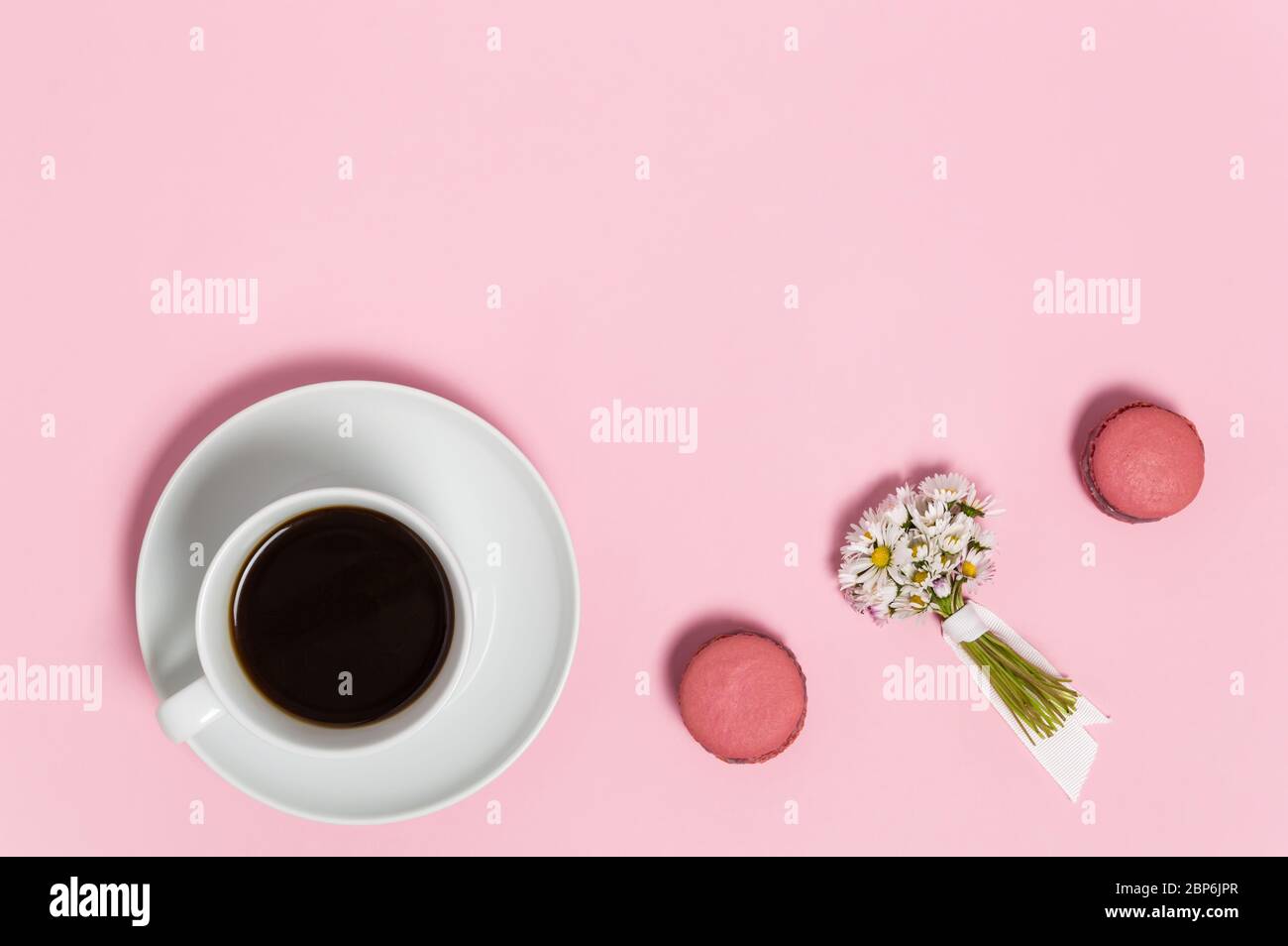 Tasse blanche de café noir, deux macarons français roses et bouquet de fleurs de Marguerite tendres sur fond rose. Gros plan sur le magnifique romantique bre Banque D'Images
