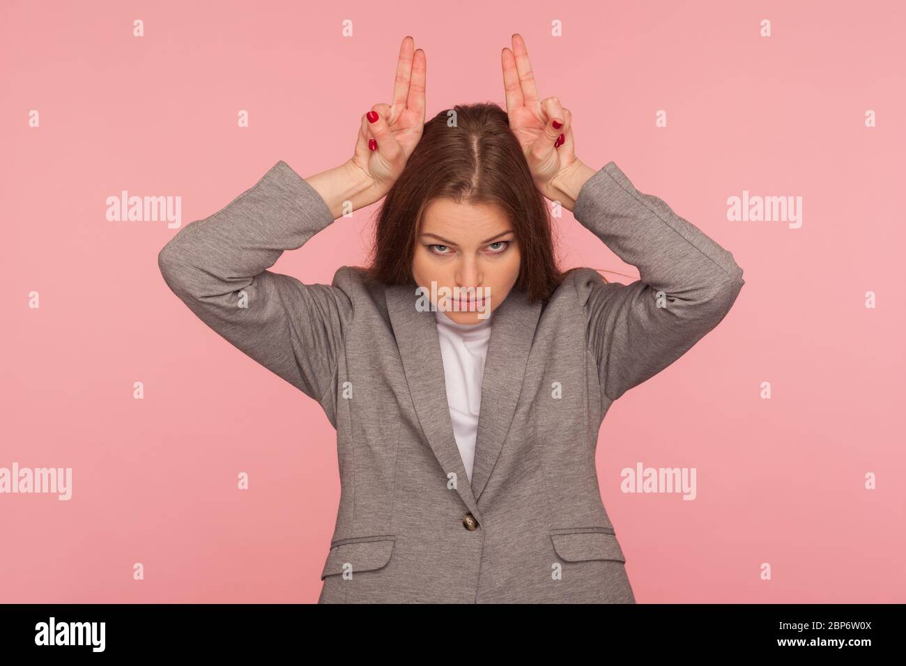 Je suis dangereux! Portrait de jeune femme agressive en costume d'affaires debout avec le signe de la main de corne de taureau, le geste de fourmis sur la tête, menaçant d'attaquer e Banque D'Images