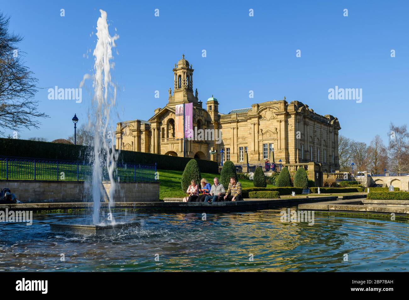 Extérieur de la galerie d'art Cartwright Hall (grand bâtiment historique) et 4 personnes assises près de la fontaine du jardin aquatique Mughal - Lister Park, Bradford, Angleterre, Royaume-Uni Banque D'Images