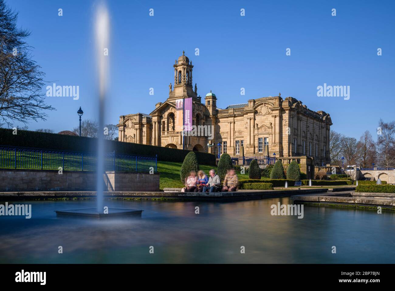 Extérieur de la galerie d'art Cartwright Hall (grand bâtiment historique) et 4 personnes assises près de la fontaine du jardin aquatique Mughal - Lister Park, Bradford, Angleterre, Royaume-Uni Banque D'Images