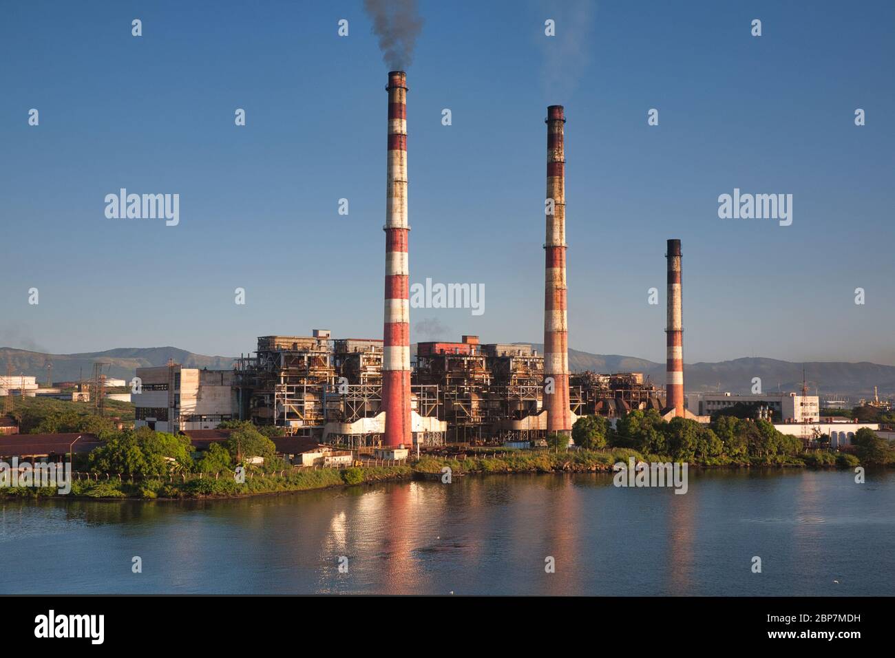 Santiago de Cuba sur la côte sud de Cuba. Une centrale électrique avec trois cheminées reflétées dans l'eau de l'entrée sur laquelle elle se trouve Banque D'Images