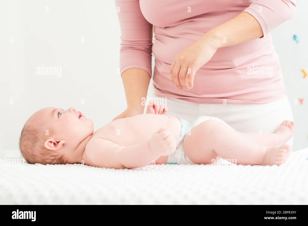 Mere Debout A Cote De Lit Avec Son Nouveau Ne Garcon Couche Sur Son Dos Bebe Garcon Sur Un Lit Portant Une Couche A La Recherche A La Mere Et Souriant Photo Stock