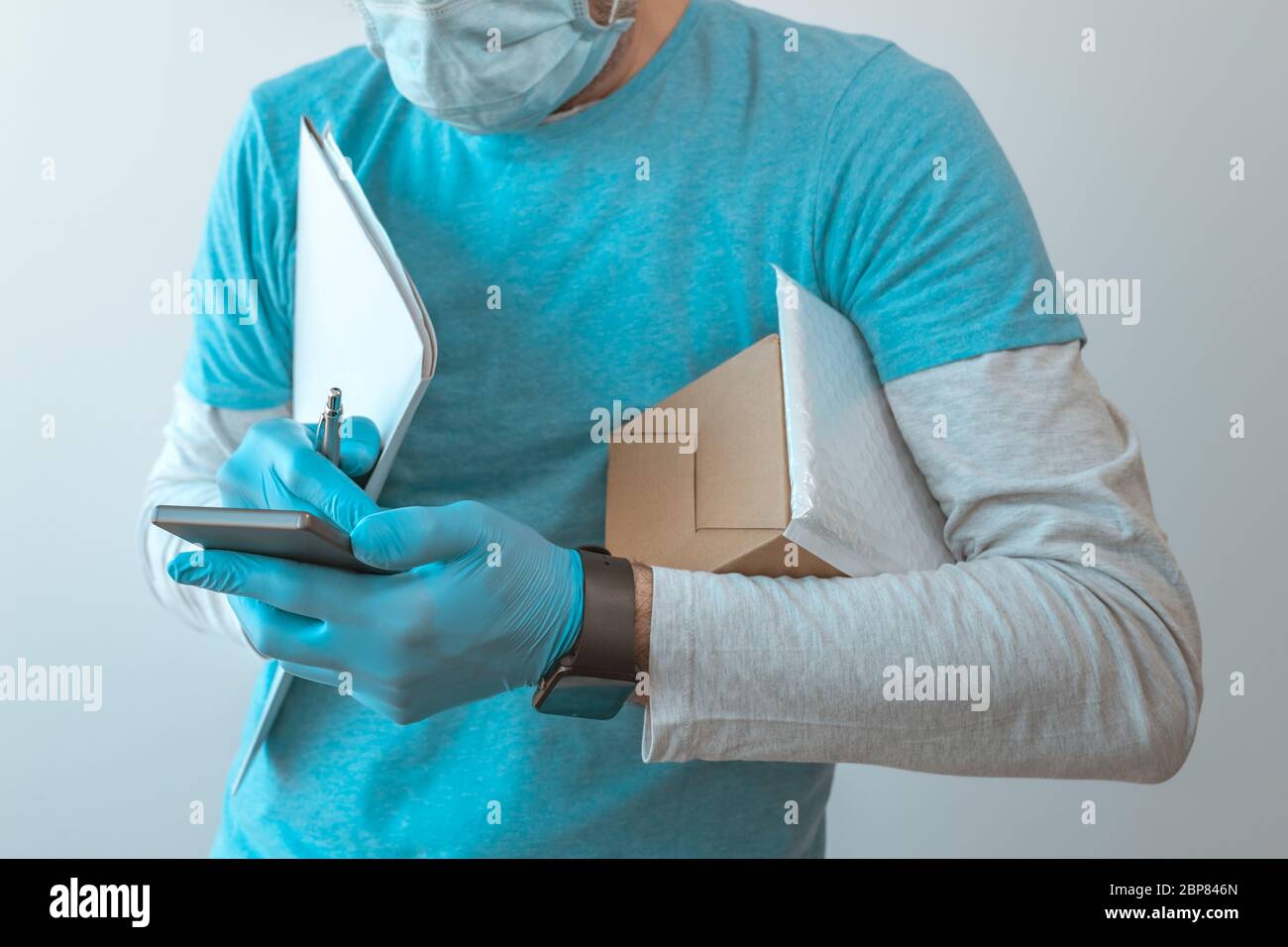 Homme de livraison avec des vêtements de protection utilisant un smartphone avec des gants de protection pendant une pandémie d'infection virale, foyer sélectif Banque D'Images