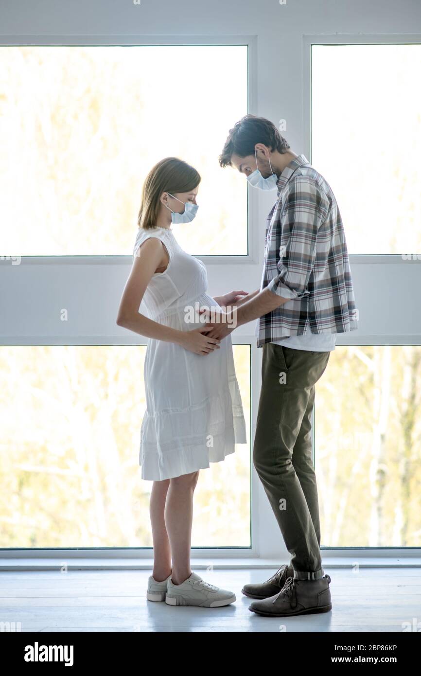 Homme grand dans un masque touchant l'abdomen enceinte de sa femme et se sentant excité Banque D'Images