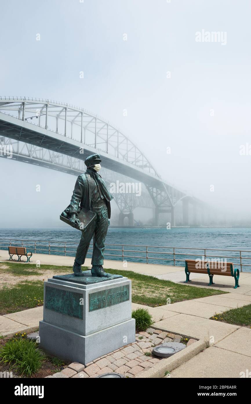 Statue du jeune Thomas Edison portant un masque chirurgical devant les ponts internationaux Blue Water doubles en une journée de brouillard. Banque D'Images