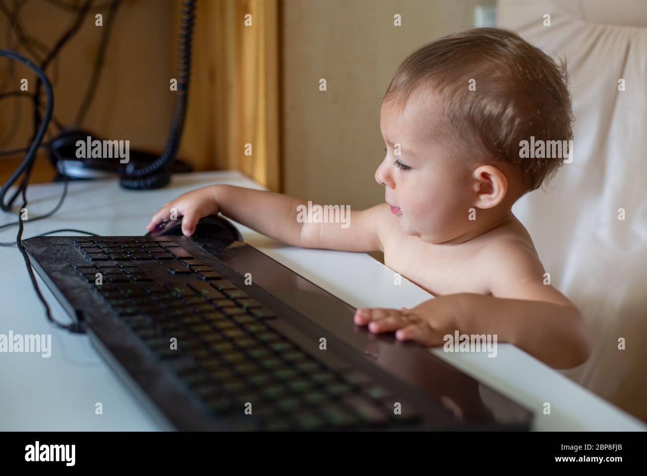 Petit Bebe Mignon Assis Sur Une Chaise De Bureau Et Avant Le Clavier Noir Et Met La Main Sur La Souris Noire Il Travaille Gros Plan Doux Foyer Photo Stock Alamy