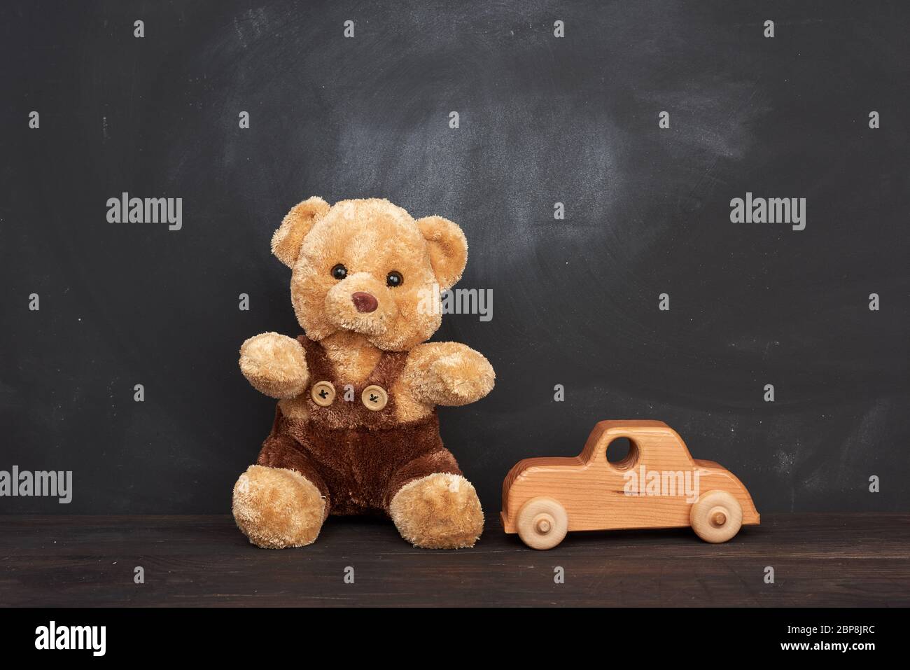 l'ours en peluche brun est assis sur une table en bois marron et une voiture en bois, derrière un tableau noir vide, un endroit pour une inscription, de retour à l'école Banque D'Images