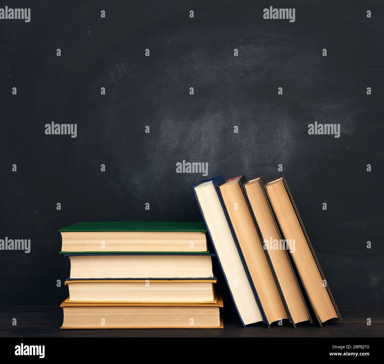 pile de divers livres de hardback sur le fond d'un tableau noir vide de craie, place pour le texte, de retour à l'école Banque D'Images