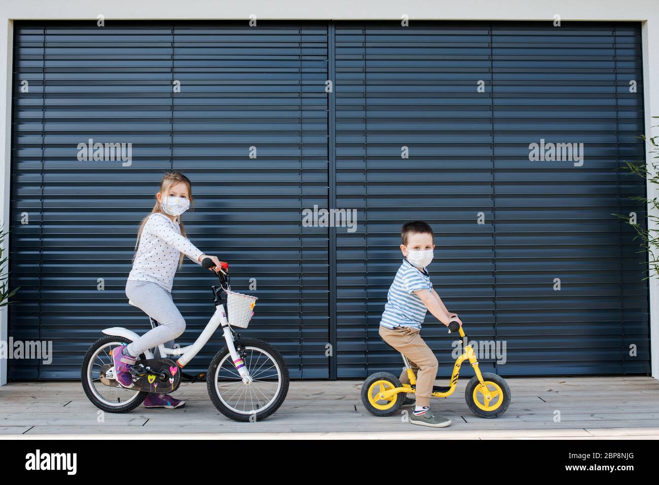 Petite fille et garçon avec des vélos à l'extérieur à la maison. Virus Corona et concept de quarantaine. Banque D'Images