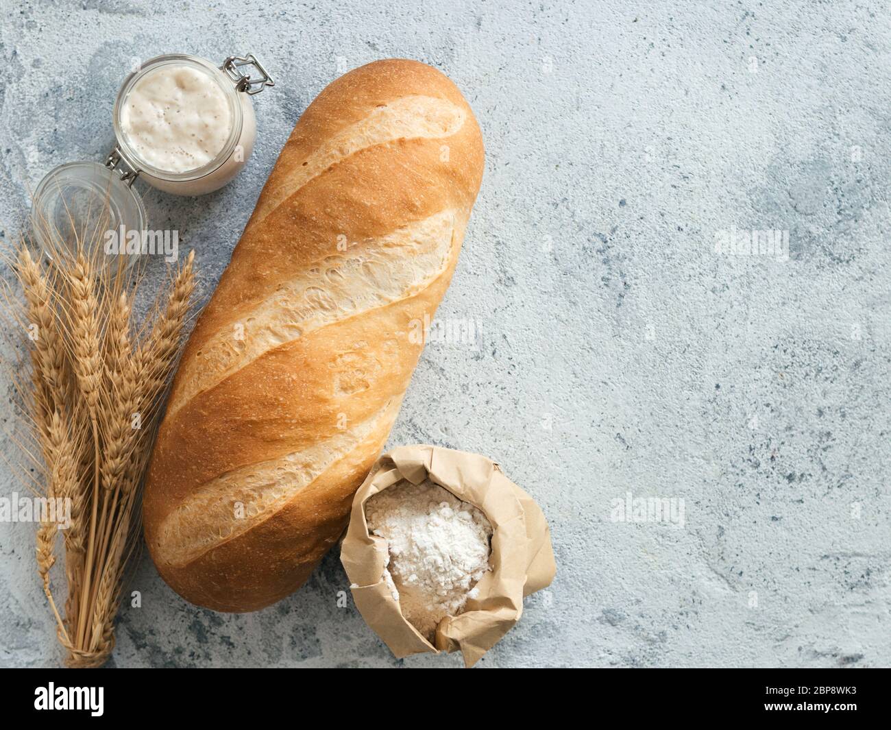 Pain de pain de Bomer blanc britannique ou de levain européen sur fond de ciment gris. Pain frais et pot en verre avec levain, farine dans un sac en papier et oreilles. Vue de dessus. Copier l'espace Banque D'Images