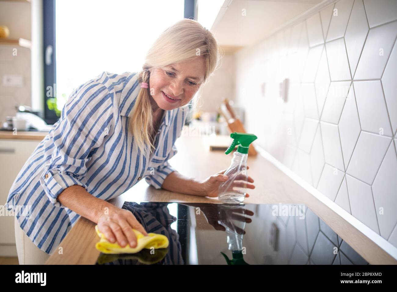 Portrait d'une femme âgée qui nettoie une plaque vitrocéramique dans la cuisine à l'intérieur de la maison. Banque D'Images