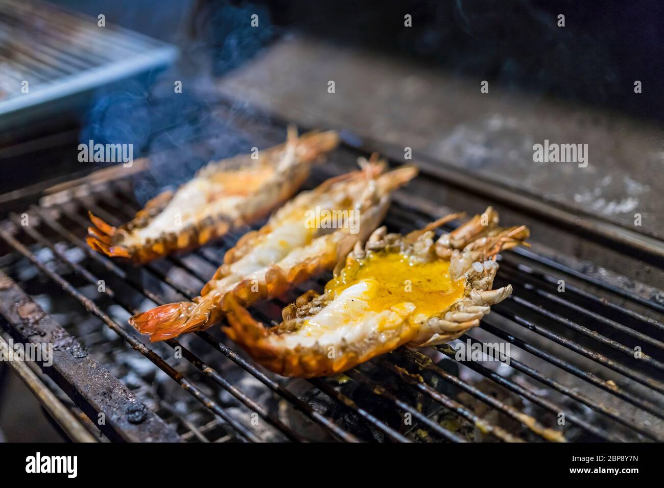 3 grosses crevettes grillées sur le barbecue. La fumée s'élevant dans la nuit. Propose de la nourriture thaïe. Focus sélectif. Banque D'Images
