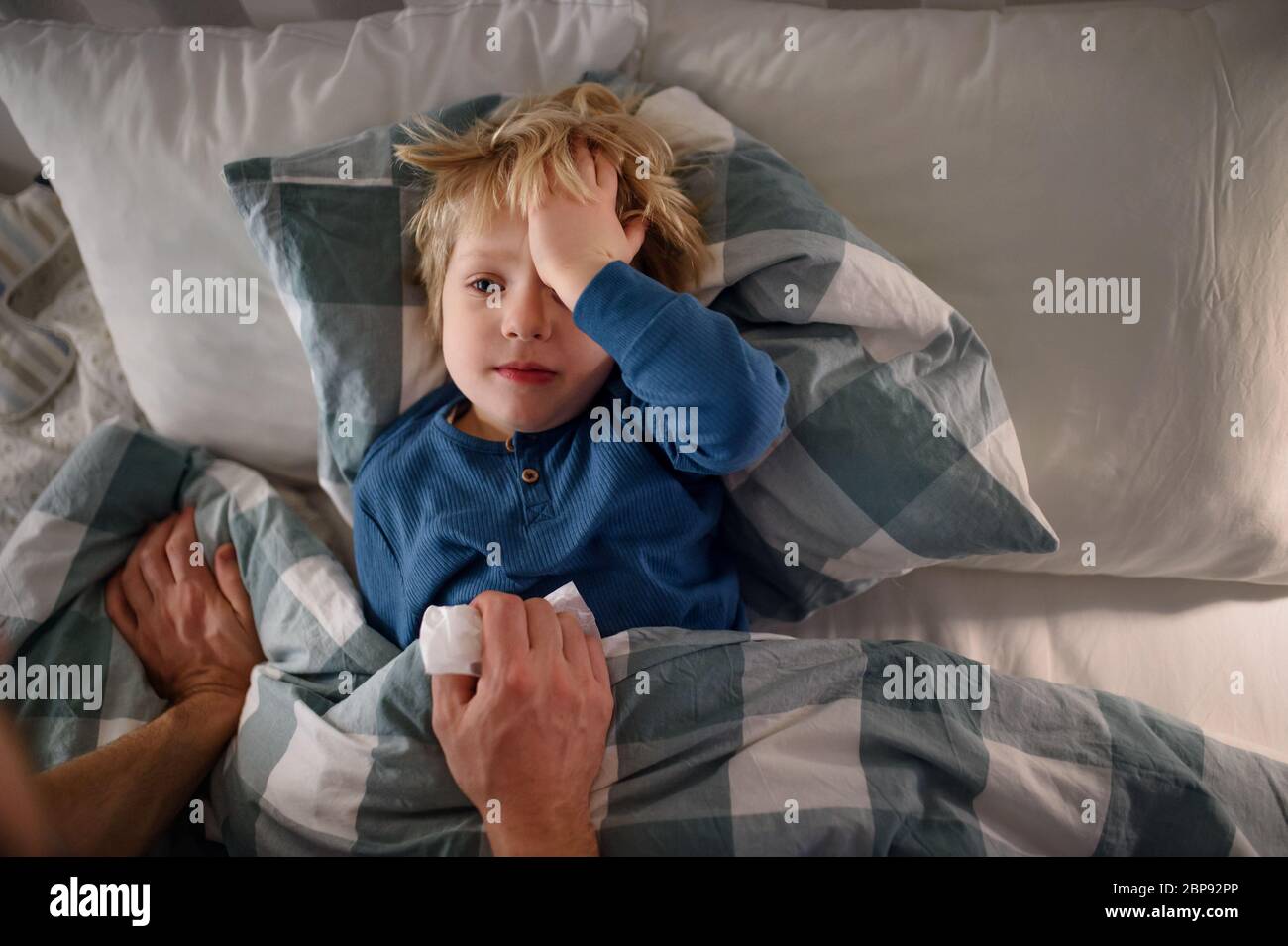 Le père s'est fait soigner sur un petit fils malade allongé dans un lit à l'intérieur à la maison. Banque D'Images