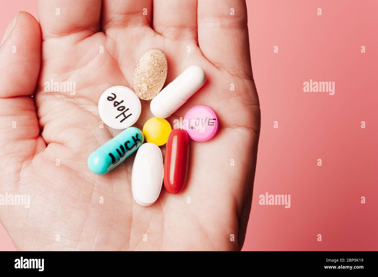 Le concept de pilules créatives, un placebo dans la main, avec joie, amour, bonheur, vérité, pouvoir, rêve sur fond rose Banque D'Images