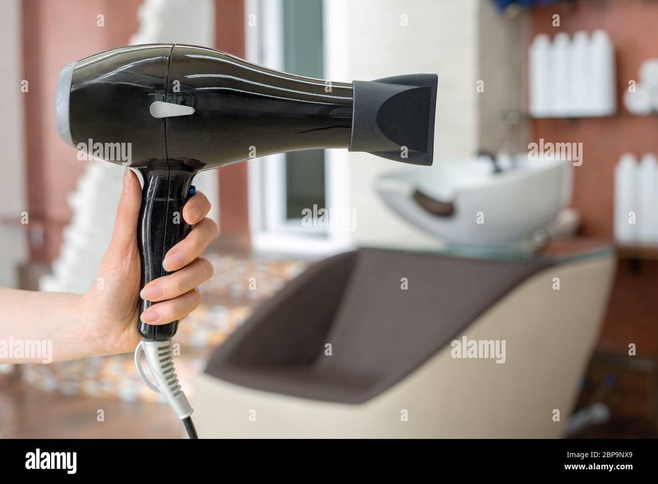Sèche-cheveux professionnel commode à cheveux outil dans la main de coiffeur contre le fond intérieur de salon de beauté. Espace de travail du coiffeur. Coiffure de beauté Banque D'Images