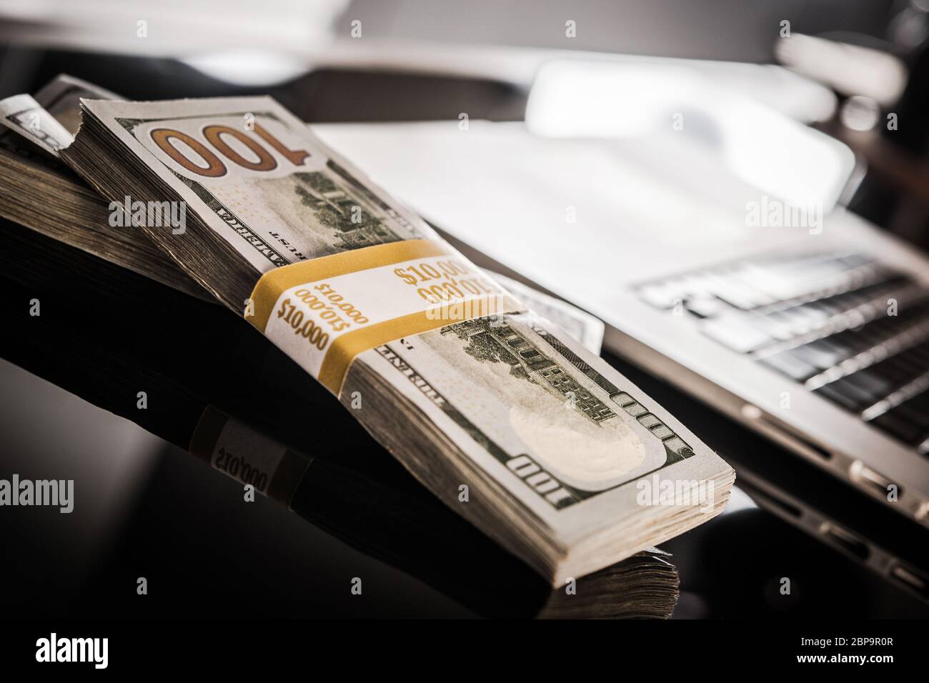 Vingt mille dollars en deux ensembles sur une table en verre près d'un ordinateur portable. Banque D'Images