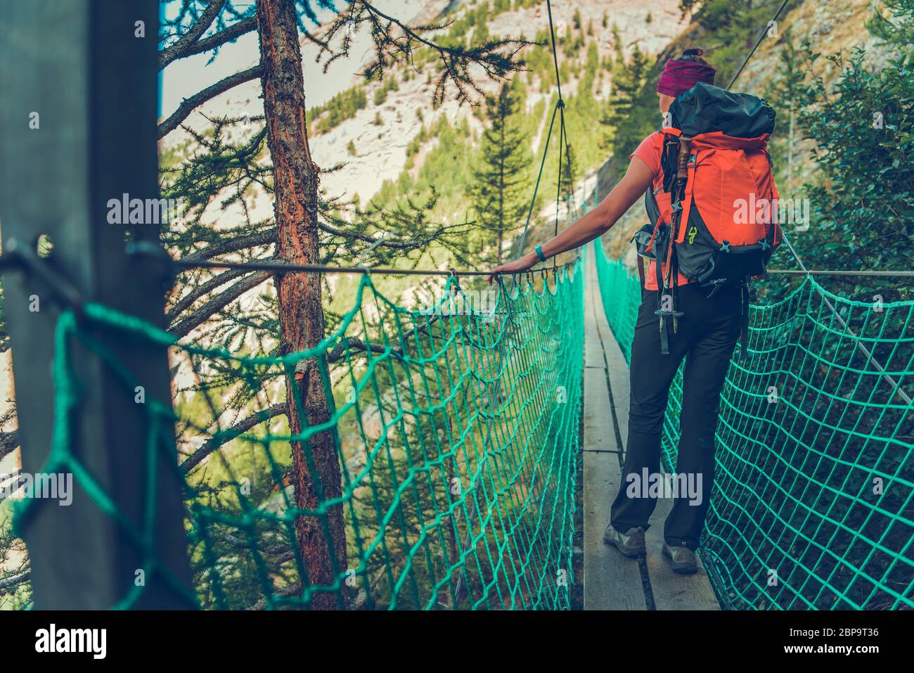 Caucasiens Femme Backpacker marchant à travers le pont étroit de suspension dans les montagnes. Banque D'Images