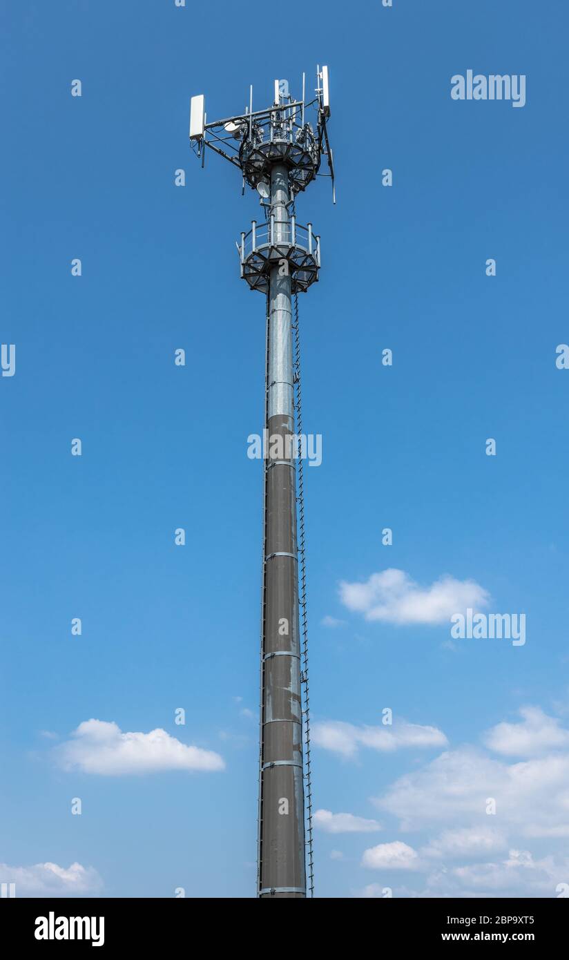 Une tour de communications pour les signaux de téléphones mobiles, contre un fond de ciel bleu avec des nuages blancs. Banque D'Images