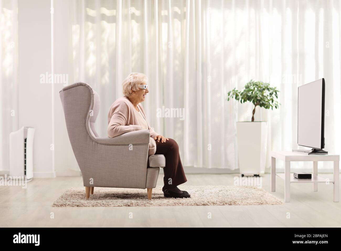 Femme âgée avec une paire de lunettes 3D assise dans un fauteuil et regardant la télévision à la maison Banque D'Images