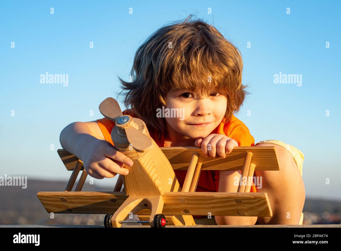 Un enfant heureux rêve de voyager et de jouer avec un avion jouet. Petit pilote aviateur en extérieur sur fond bleu ciel d'été. Rêves d'enfant Banque D'Images