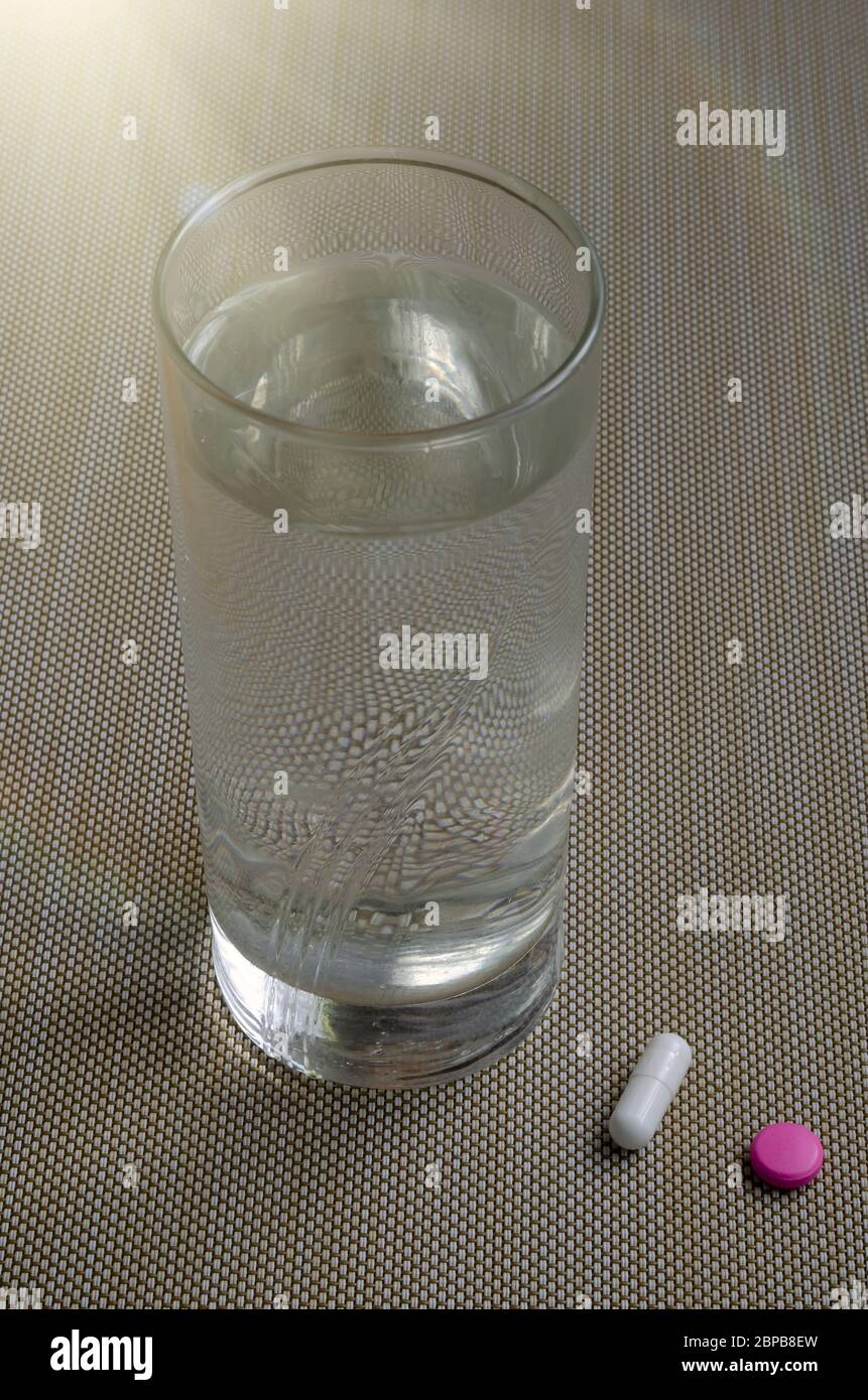 Pilules médicales et un verre d'eau sur fond beige texturé. Une pilule rose, une pilule blanche et un verre d'eau. Soins de santé, médicaments. Fermer Banque D'Images