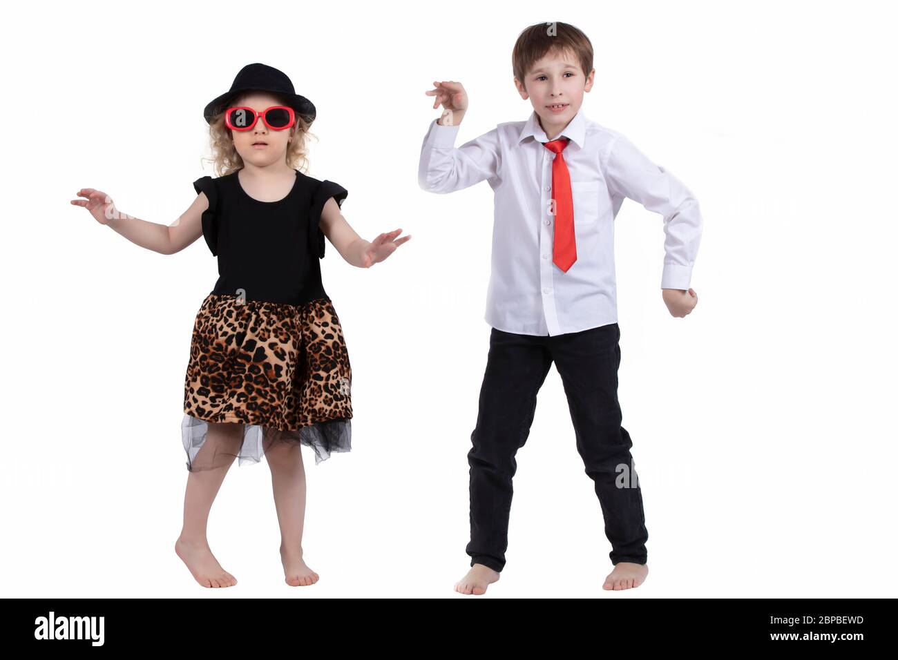 Enfants amusants dansant sur fond blanc. Une petite fille dans un chapeau et un garçon dans une cravate dansent. Danse de salle de bal. Couple de danse Banque D'Images