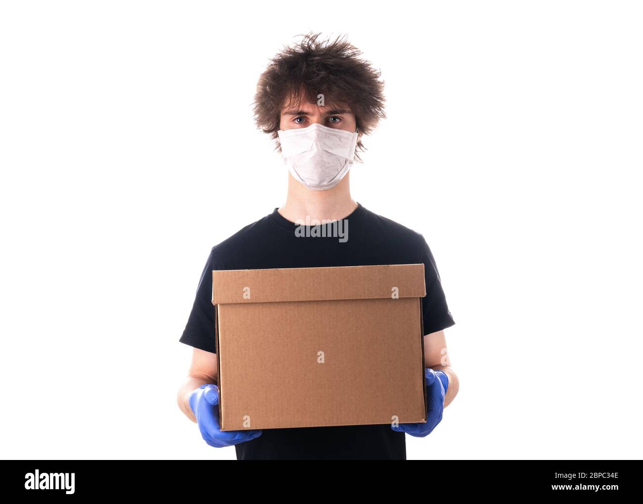 un jeune homme dans un masque et un t-shirt noir et des gants en latex tient une boîte en carton pour la livraison isolée sur fond blanc. Boîte de dons. Livraison Banque D'Images