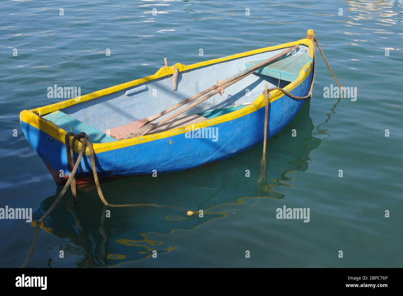 Un petit barque flotte dans le port de Marsaxlokk, un village de pêcheurs traditionnel sur la côte sud-est de l'île de Malte. Banque D'Images