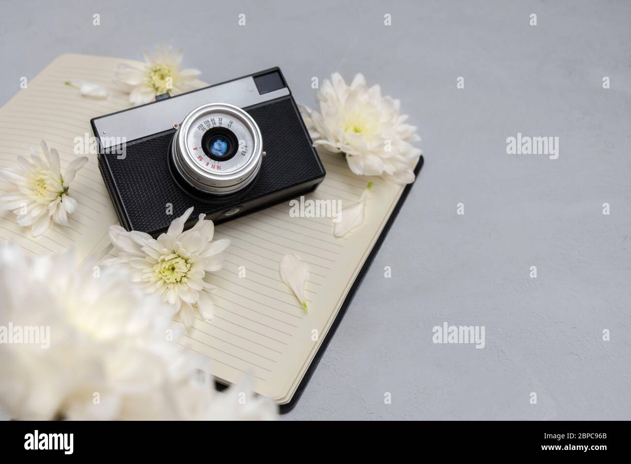 Ancien appareil photo rétro avec beau bouquet de fleurs blanches et bloc-notes vierge sur fond neutre. Expérience blogueur ou photographe Banque D'Images