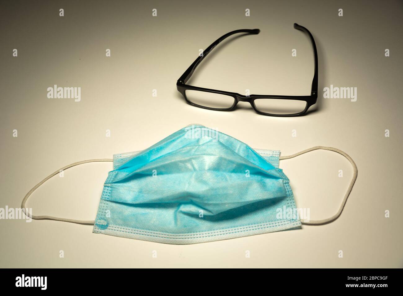 Masque chirurgical bleu et lunettes noires sur fond blanc Banque D'Images